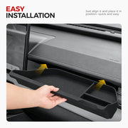 Hand installing a black rubberized car center console organizer tray into a vehicle dashboard.